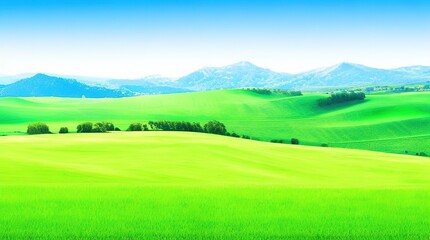 Fototapeta premium Scenic view of green grass fields and rolling hills under a clear blue sky with distant mountains and fluffy clouds