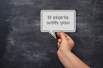 A hand holding a paper that says It starts with you.