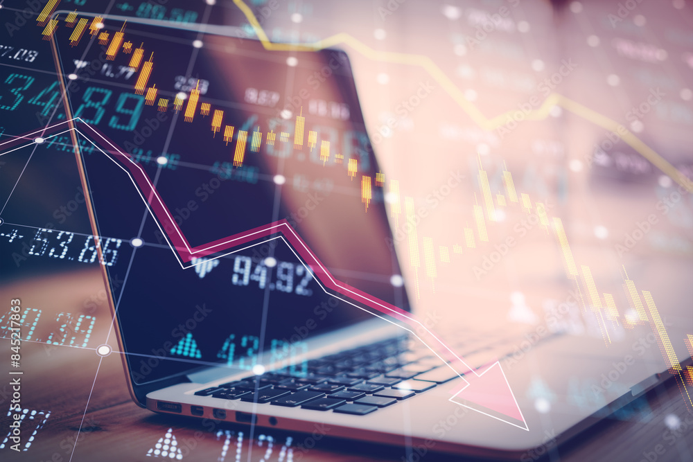 Poster close up of office workplace with laptop and glowing falling forex chart and index grid on blurry ba