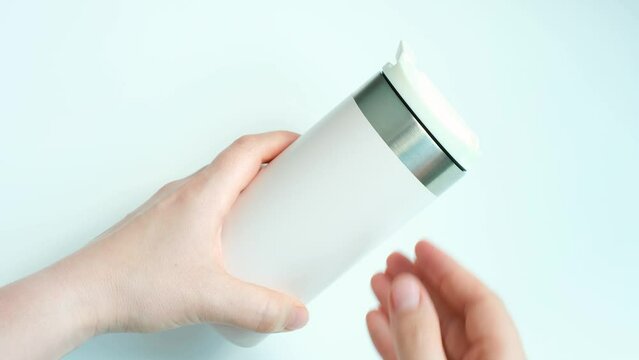 Female hands open thermo mug on white background top view close-up.