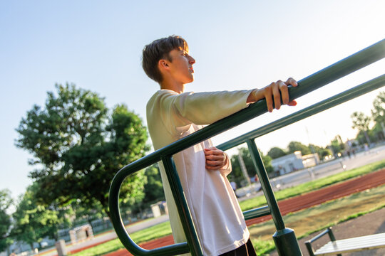 Young Man Leaning on Parallel Bars at Outdoor Park on Sunny Day