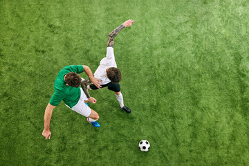 Fototapeta premium Aerial view. Dynamic photo of young football athletes in different uniform playing game on green lush playground. Concept of professional sport, championship, final match, movement. Ad
