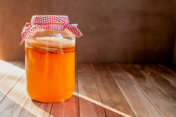 homemade fermented drink Kombucha in a glass jar on wooden table.