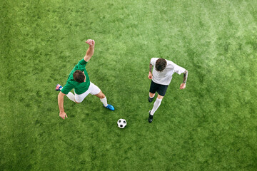 Aerial view. Two players in white and green uniforms battle for the ball on green lush playground. Concept of professional sport, championship, final match, movement. Ad