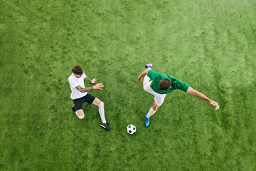 Fototapeta premium Aerial view. Two athletic men, soccer players playing in motion on green lush playground. Moment from football match. Concept of professional sport, championship, final match, movement. Ad