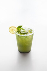 Mint lemonade shikanjabeen served in a plastic to go cup with mint leaves ice cubes and slice of lemon on a white background.