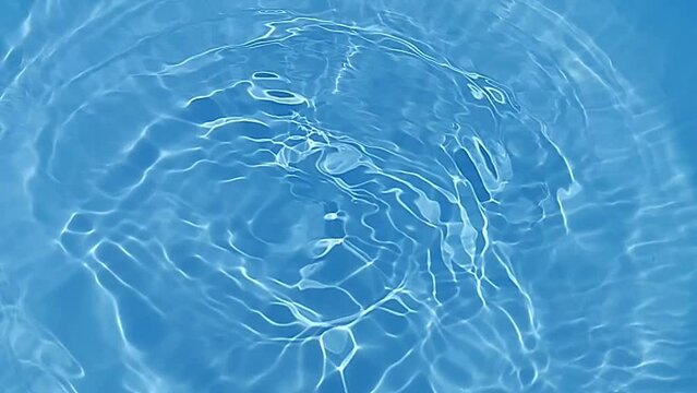 Blue water with ripples on the surface. Defocus blurred transparent blue colored clear calm water surface texture with splashes and bubbles. Water waves with shining pattern texture background.