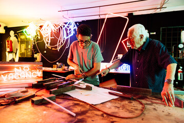 Father Teaching Son Neon Sign Bending Techniques in Family-Run Workshop