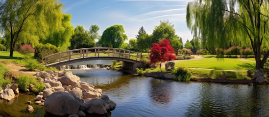 Fototapeta premium A picturesque park with a kids playground and a charming bridge over a shimmering creek captured in a sunny day panoramic image with plenty of empty space. Creative banner. Copyspace image