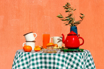 Orange juice with cups near red colored tea kettle on table at terrace