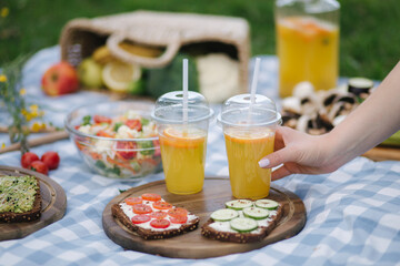 Woman take fresh orange juice on vegan picnic outdoors, Picnic on blue checkered blanket in park. Healthy food concept