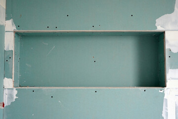 A wall covered with green plasterboard, in which a built-in niche.