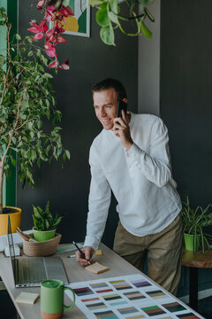Smiling interior designer talking on smart phone and working at desk in office