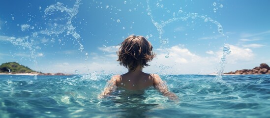 A boy child playing in the sea waves enjoying the summer vacation with water splashes as seen from the back Ideal for a copy space image 167 characters