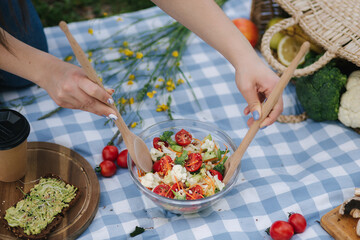 Woman mixes vegan salad on picnic outside. Vegan food concept