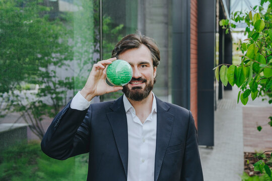 Businessman covering eye with puzzle sphere near office building 