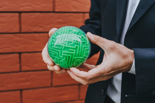 Businessman holding puzzle sphere near brick wall