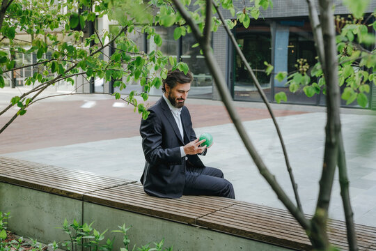 Businessman solving puzzle sphere and sitting on bench at office park