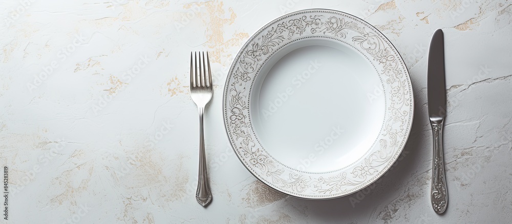Poster A white dinner plate sits on a white marble surface featuring intricate patterns A shiny silver spoon completes the composition The image offers ample copy space