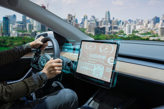 Person driving an electric car with a futuristic, high-tech dashboard and city skyline in the background.