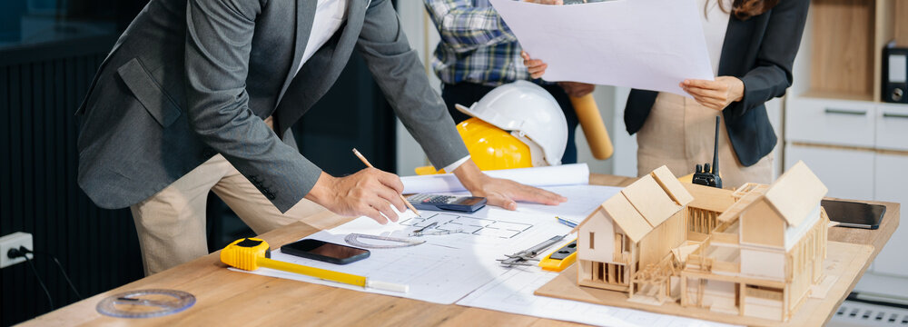 Engineer teams meeting working together wear worker helmets hardhat with on architectural project site and making model house. Asian industry professional team