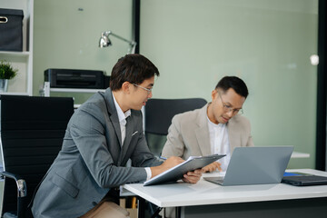 Happy Asian businesspeople while collaborating on a new project.  using a laptop and tablet