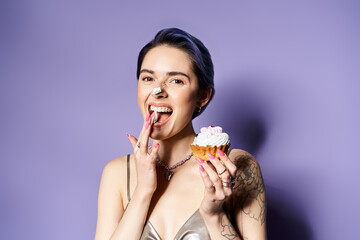 Young woman with short blue hair holding cupcake in front of mouth, dressed in silver party attire.