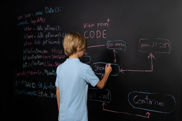 Back view of boy writing a code on blackboard while stand and think with casual shirt and holding...