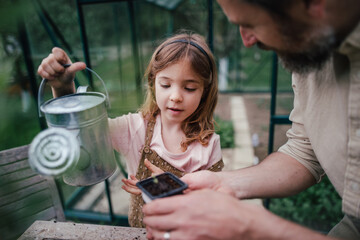 Fater and girl working together in garden, watering seedlings, spending time togeter, have shared...