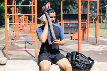 Attractive Young Asian Athlete Resting After Workout Outdoors While Sitting And Wiping Face With Towel