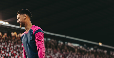 Professional goalkeeper in action during a football game at a big stadium with a smiling expression