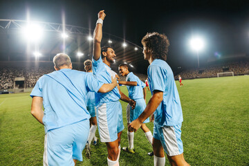 Professional football players celebrating victory at a stadium match under bright lights