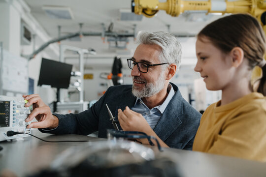 Father and girl during take your daughter to work day, encouraging girl in career in robotics. Teacher showing young schoolgirl how to assemble small robot. - Powered by Adobe
