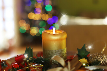 Świąteczna świeca z cynamonem, szyszkami, jabłkiem i innymi ozdobami na tle świątecznej świecącej choinki. Świąteczny nastrój © Anna