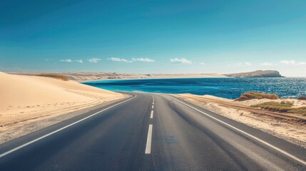 Empty highway on the background of huge sand dunes and sea coast on one side of the road, blue water, clear sunny day, bright rays, incredible nature