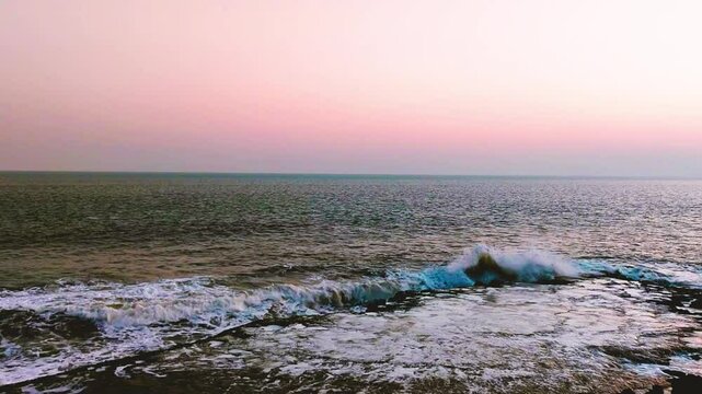 Water waves of beach hitting large stone, evening time.