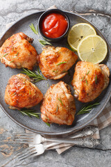 Lemon rosemary chicken thighs served with ketchup close-up in a plate on the table. Vertical top view from above