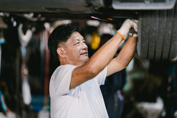 Happy Asian Mechanic man Working Repair Vehicle in Car Service. Worker fixing suspension system undercar.