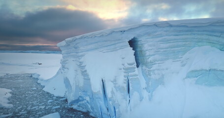 Huge high ice glacier panorama under sunset sky. Polar nature environment. Arctic winter landscape. Snow covered blue iceberg, ice wall in frozen ocean. Antarctica travel and exploration. Drone shot
