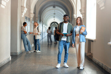 College students with diverse backgrounds socializing in university hallway with books and tablets