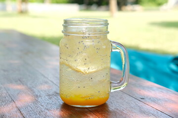 Refreshing mango mojito in a glass jar with ice and chia seeds, set on a wooden table in a sunny...