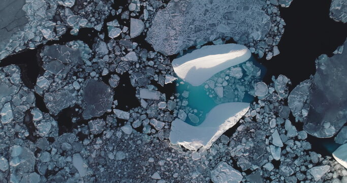 Melting glacier in frozen polar ocean aerial top down. Blue water iceberg floating in Antarctic broken ice. Global warming and climate change. Beauty nature winter landscape. Drone rotation panorama