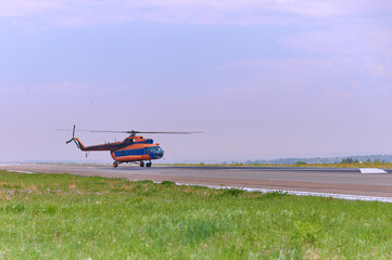 Orange helicopter on a green meadow with yellow flowers preparing to take off. Sunny summer day....