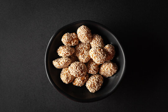 Top view of a black bowl filled with Indian sweet item called 'Rewri' or 'Revdi' or Sesame seeds sweet, on a black background.