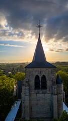 Obraz premium A historic stone church tower stands under a dramatic sunset, surrounded by lush greenery and a serene ambiance