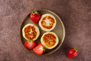 Vegan cheesecakes, syrniki, cheese pancakes with strawberries, cashew and tofu on a brown table. Sugar, lactose and gluten free. Top view.