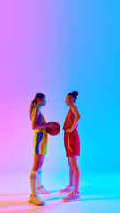 Full-length. Women, basketball players, opponents standing and looking at each other with focus against gradient pink blue background in neon. Concept of sport, active lifestyle, competition, game