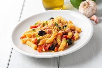 Piatto di fusilli conditi con prosciutto, olive nere e sugo, pasta italiana, gastronomia europea 
