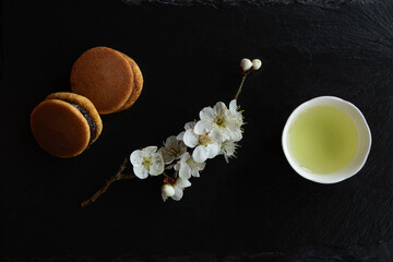 Dorayaki, Traditional Japanese sweets, Ume (apricot) flower branch and Japanese green tea in a beauty minimalist aesthetic arrangement on black granite board background. Japan.