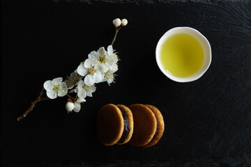 Dorayaki, Traditional Japanese sweets, Ume (apricot) flower branch and Japanese green tea in a beauty minimalist aesthetic arrangement on black granite board background. Japan.